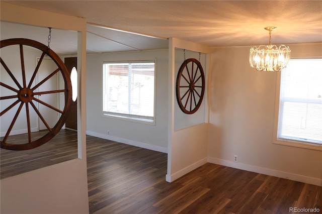 spare room featuring dark wood-type flooring and a chandelier