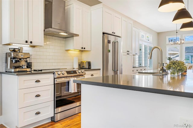 kitchen featuring white cabinets, wall chimney exhaust hood, appliances with stainless steel finishes, and hanging light fixtures