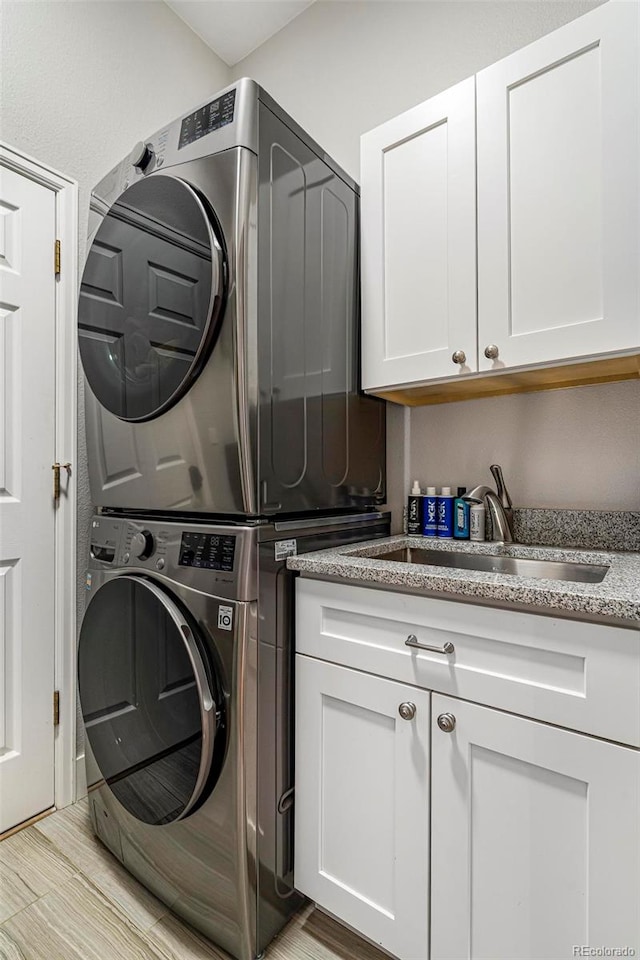 laundry room featuring sink, light wood-type flooring, cabinets, and stacked washer and clothes dryer