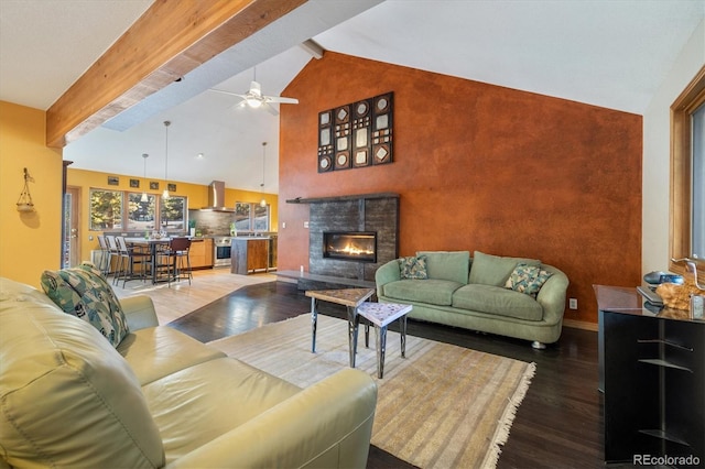 living room with ceiling fan, wood finished floors, baseboards, beamed ceiling, and a glass covered fireplace