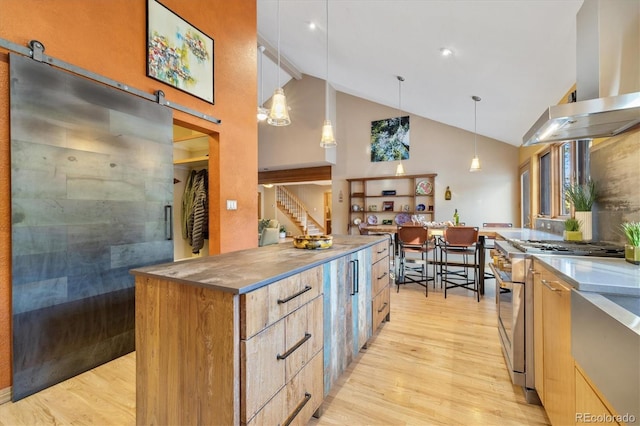 kitchen featuring a barn door, wall chimney range hood, high end stainless steel range, light wood-type flooring, and pendant lighting