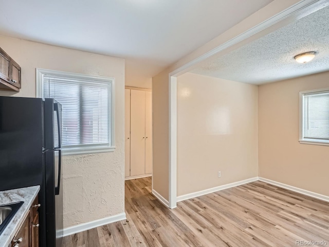 kitchen featuring dark brown cabinets, light wood-type flooring, black fridge, and a healthy amount of sunlight