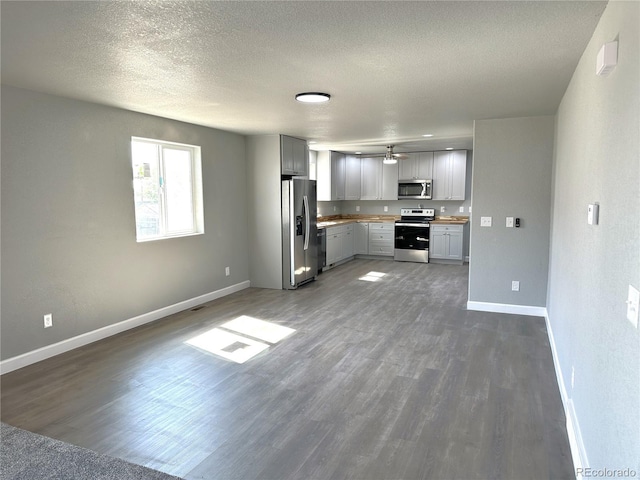 kitchen with dark wood finished floors, gray cabinetry, appliances with stainless steel finishes, a textured ceiling, and baseboards