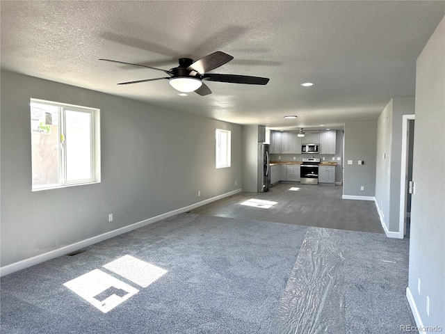 unfurnished living room featuring dark carpet, a textured ceiling, and baseboards