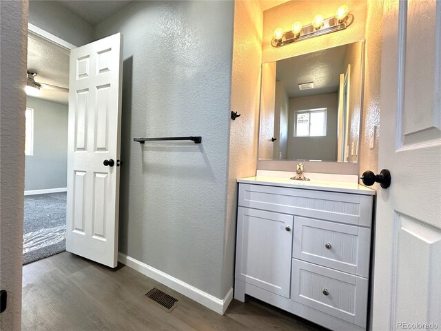 bathroom featuring a textured wall, wood finished floors, visible vents, vanity, and baseboards