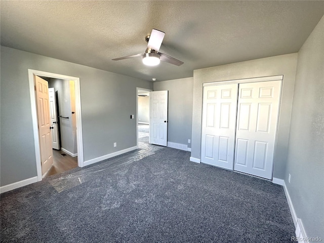 unfurnished bedroom featuring dark colored carpet, a closet, a textured ceiling, and baseboards