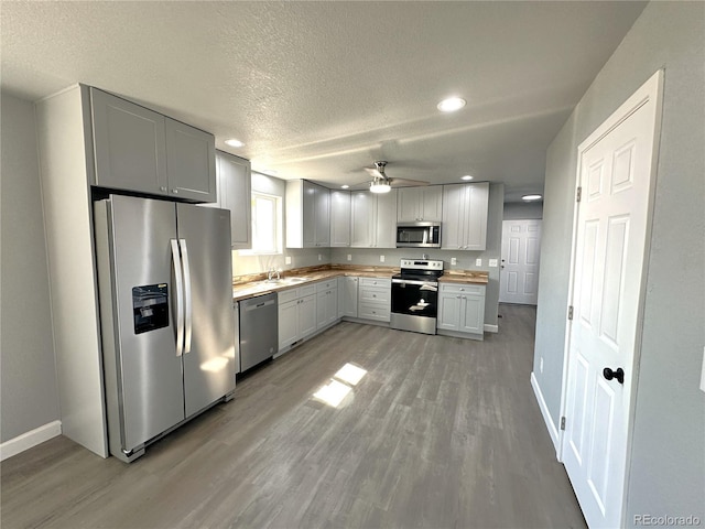 kitchen featuring a textured ceiling, stainless steel appliances, a sink, baseboards, and light wood-style floors