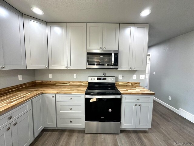 kitchen featuring baseboards, dark wood finished floors, butcher block counters, stainless steel appliances, and recessed lighting