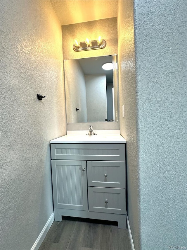 bathroom featuring a textured wall, vanity, baseboards, and wood finished floors