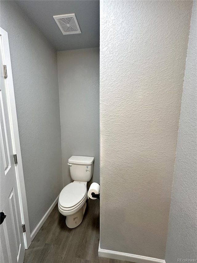 bathroom featuring visible vents, a textured wall, toilet, wood finished floors, and baseboards