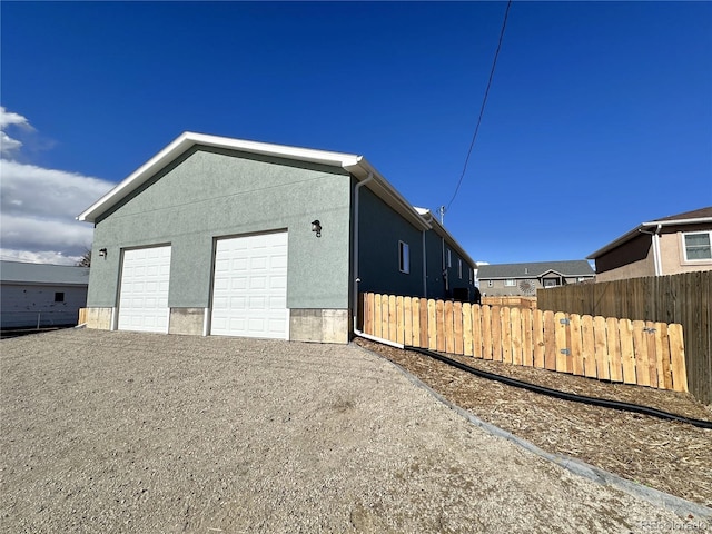 view of side of property featuring a garage, fence, gravel driveway, and stucco siding