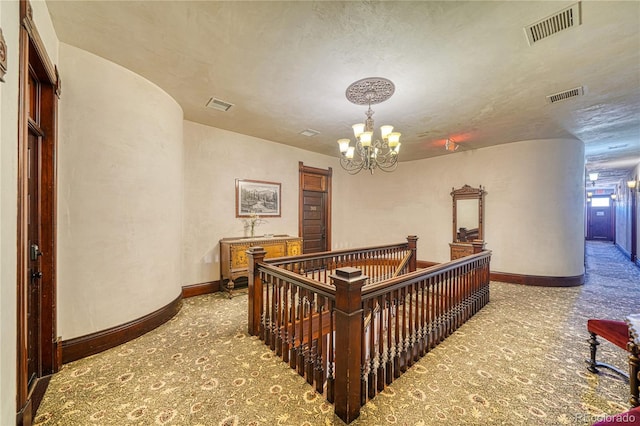 hallway with a textured ceiling, carpet flooring, and a notable chandelier