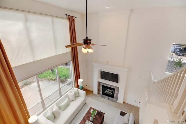 living room with ceiling fan, a towering ceiling, light carpet, and a tile fireplace