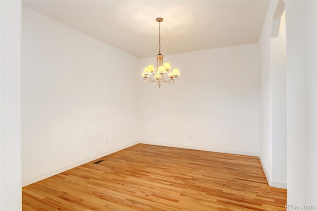 empty room with wood-type flooring and a chandelier