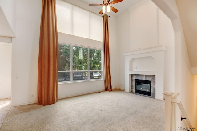 unfurnished living room with ceiling fan, light colored carpet, a fireplace, and a towering ceiling