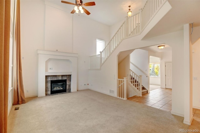 unfurnished living room featuring light colored carpet, ceiling fan, a towering ceiling, and a fireplace