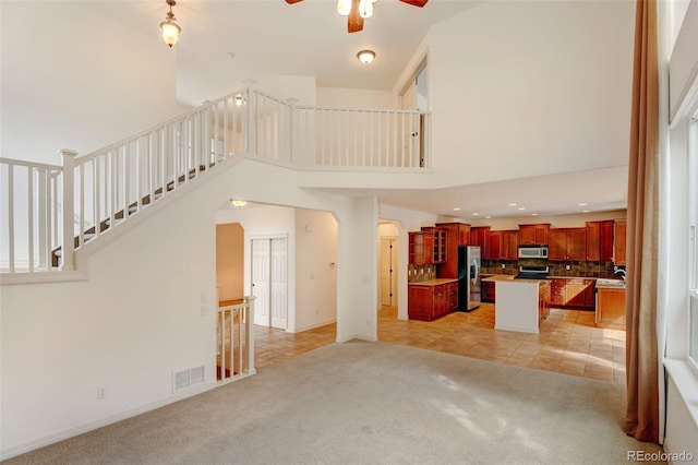 unfurnished living room with light colored carpet, ceiling fan, and a towering ceiling