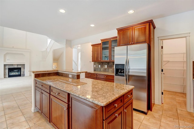 kitchen featuring light tile patterned floors, a tiled fireplace, a center island, light stone counters, and stainless steel refrigerator with ice dispenser