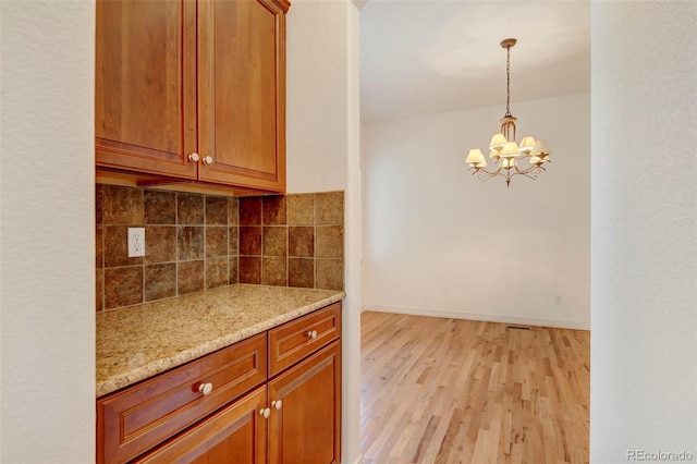 kitchen featuring backsplash, decorative light fixtures, light wood-type flooring, light stone counters, and a chandelier