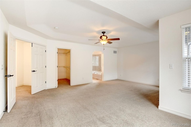 unfurnished bedroom featuring light colored carpet, a closet, a spacious closet, ceiling fan, and connected bathroom