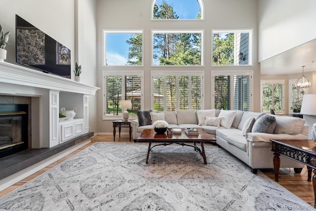 living room featuring a towering ceiling, hardwood / wood-style floors, an inviting chandelier, and a tile fireplace