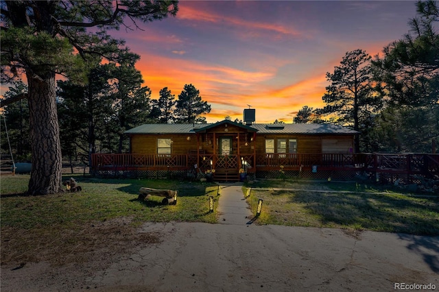 view of front of property featuring a wooden deck, a chimney, a front yard, and metal roof