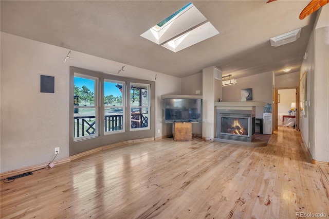 unfurnished living room featuring baseboards, a glass covered fireplace, wood finished floors, and a skylight