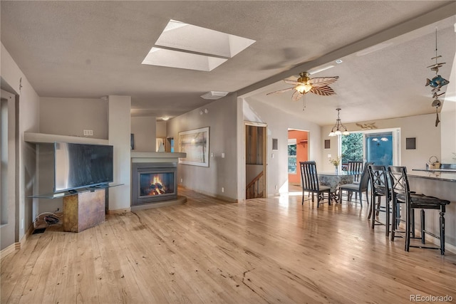 living room with hardwood / wood-style flooring, a glass covered fireplace, lofted ceiling with skylight, and a ceiling fan