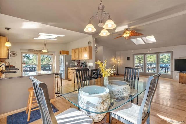 dining area with lofted ceiling with skylight, light wood-style flooring, a ceiling fan, and baseboards