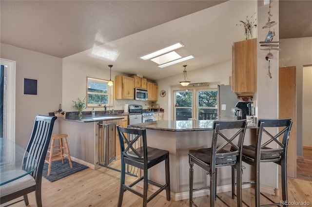 kitchen featuring light brown cabinetry, light wood finished floors, dark countertops, a peninsula, and appliances with stainless steel finishes