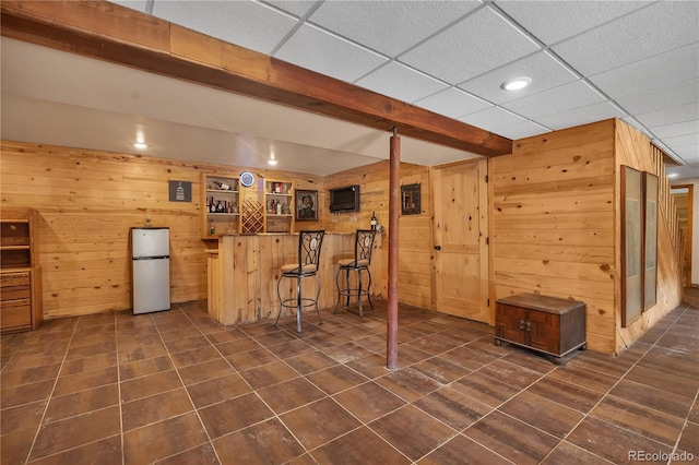 finished basement featuring dark tile patterned floors, wooden walls, freestanding refrigerator, and recessed lighting