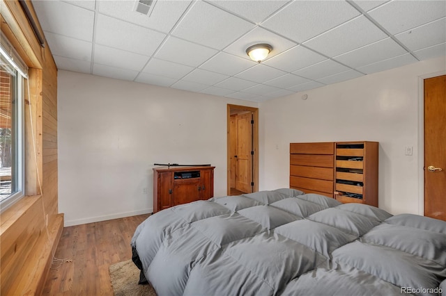 bedroom featuring wood walls, wood finished floors, visible vents, baseboards, and a paneled ceiling