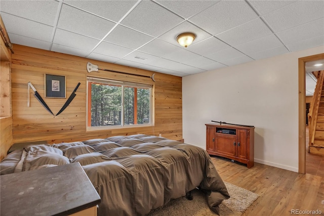 bedroom featuring light wood finished floors, wooden walls, visible vents, baseboards, and a paneled ceiling