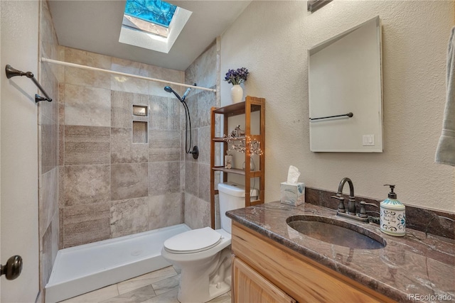 bathroom with a skylight, vanity, a textured wall, a tile shower, and toilet