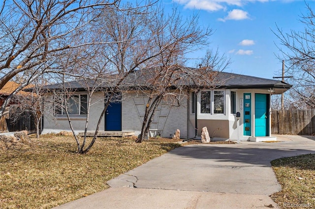 ranch-style house featuring stucco siding, driveway, fence, a shingled roof, and brick siding