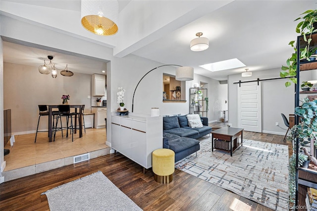 living room featuring visible vents, baseboards, a barn door, hardwood / wood-style floors, and a skylight