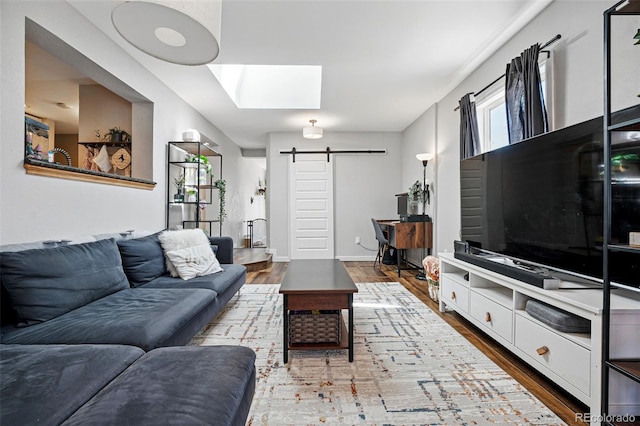 living area with baseboards, a skylight, a barn door, and wood finished floors