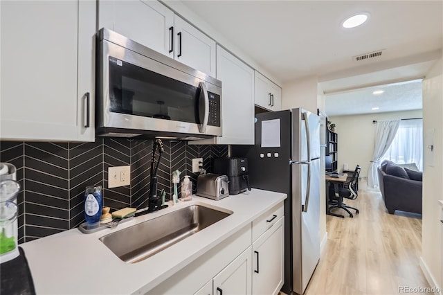 12131 Melody Dr Unit 201, Denver, CO 80234 - kitchen with stainless steel microwave, light wood-style flooring, decorative backsplash, white cabinets, and light countertops
