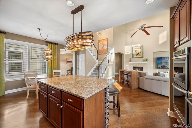 1133 Lucky Ct, Castle Rock, CO 80109 - kitchen featuring a warm lit fireplace, double oven, ceiling fan, a kitchen breakfast bar, and baseboards