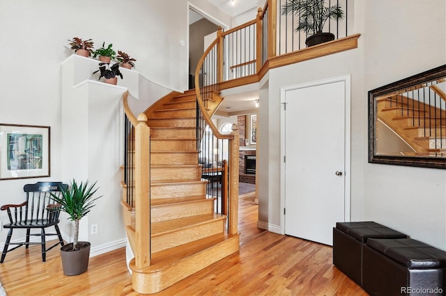 staircase featuring a brick fireplace, a towering ceiling, and hardwood / wood-style flooring