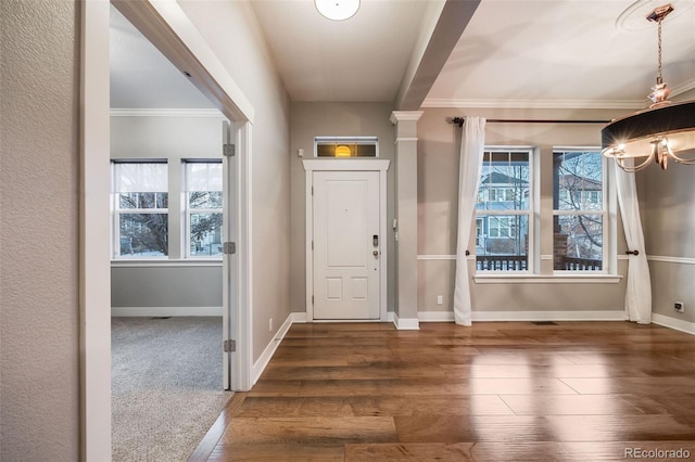 entryway with crown molding, an inviting chandelier, and dark carpet