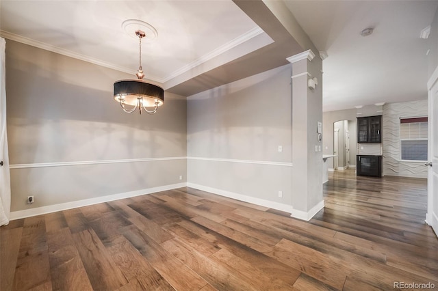 unfurnished dining area featuring ornate columns, dark hardwood / wood-style flooring, ornamental molding, and an inviting chandelier