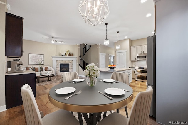 dining room with ceiling fan, a stone fireplace, and light wood-type flooring