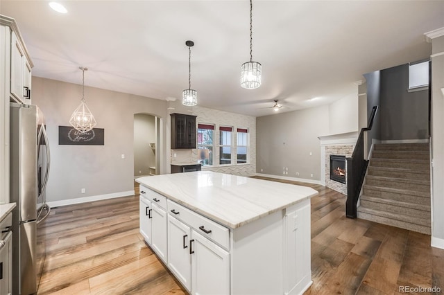 kitchen with hanging light fixtures, white cabinetry, a kitchen island, and stainless steel fridge