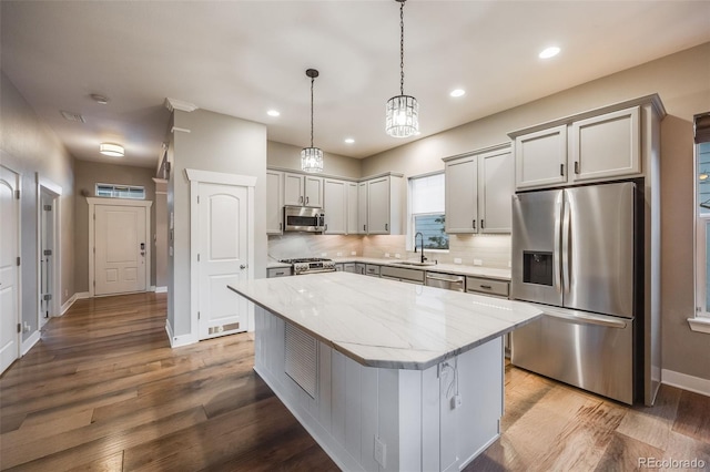 kitchen featuring a kitchen island, appliances with stainless steel finishes, pendant lighting, tasteful backsplash, and light stone counters