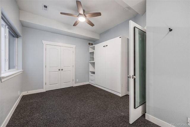 unfurnished bedroom with dark colored carpet, ceiling fan, and a closet