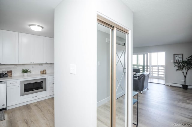 kitchen with backsplash, built in microwave, white cabinets, and light wood-type flooring