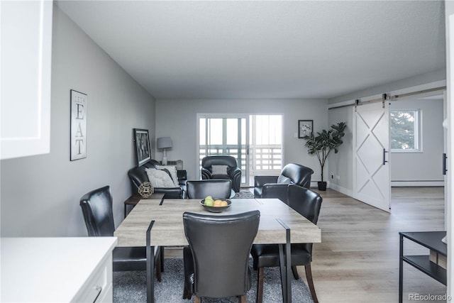 dining area featuring light wood-type flooring, a barn door, and a baseboard radiator