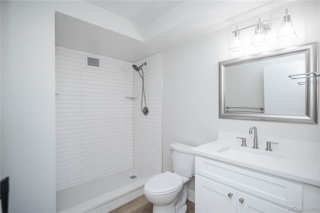 bathroom with hardwood / wood-style flooring, vanity, toilet, and a tile shower