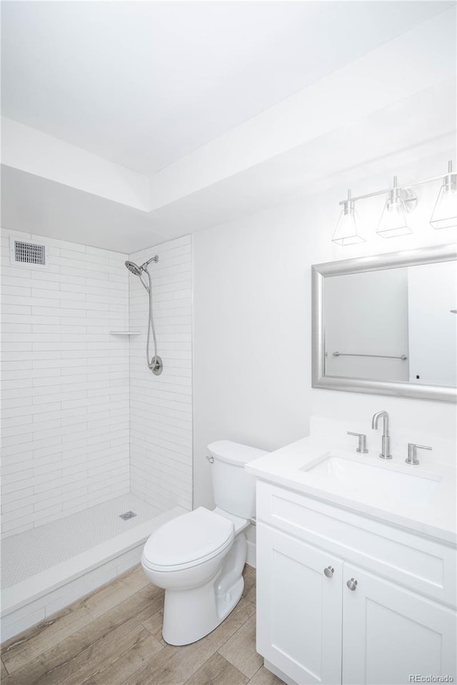 bathroom featuring tiled shower, vanity, wood-type flooring, and toilet